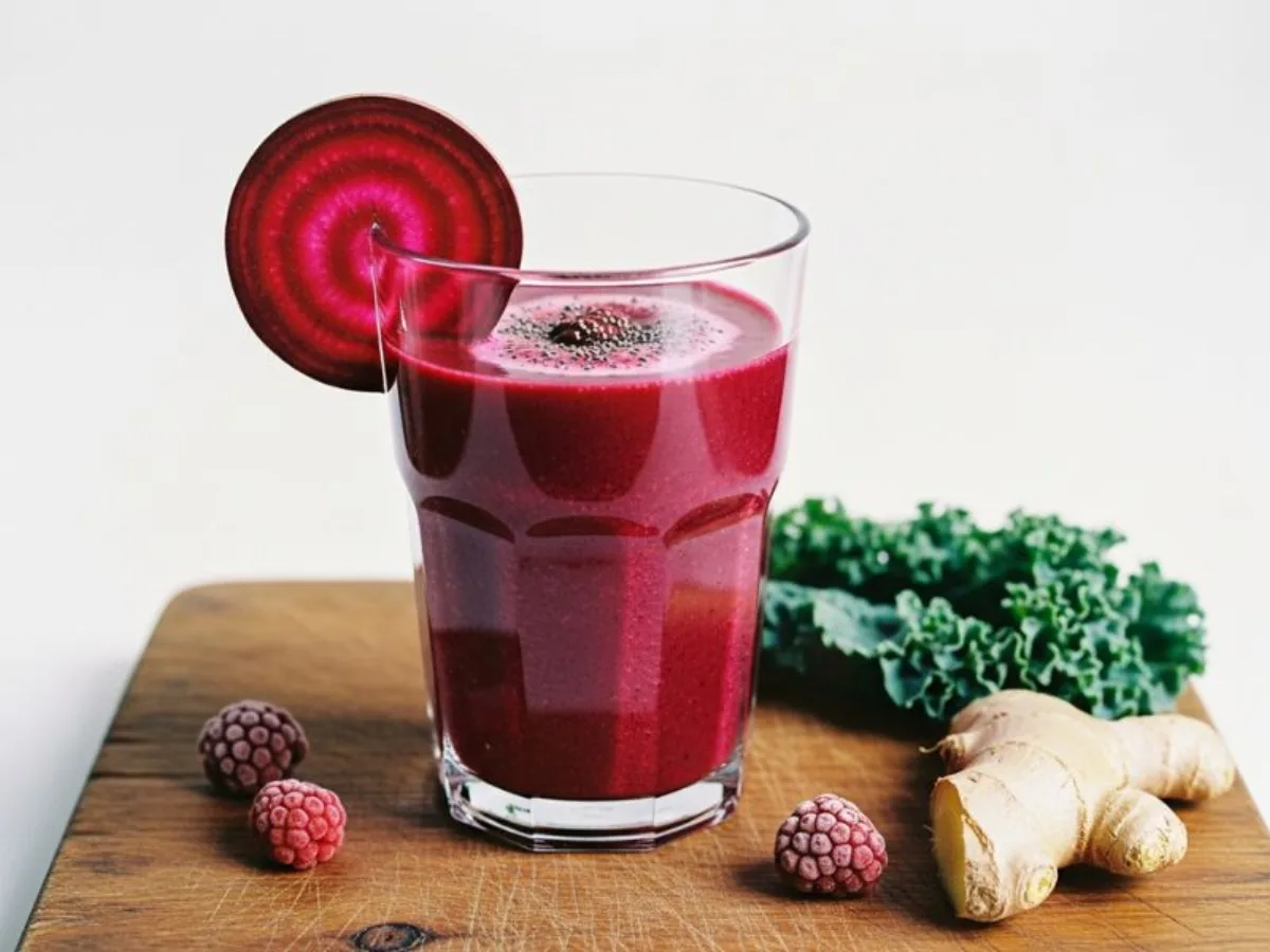 Smoothie rouge à la betterave et aux baies servi dans un grand verre, avec un morceau de gingembre frais à côté